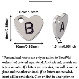 K&ouml;nnte beinhalten: Zwei silberne herzf&ouml;rmige Anh&auml;nger mit den Buchstaben "B" und "A". Der Anh&auml;nger mit "B" misst 10 mm breit und 9 mm hoch. Der Text "Add on Item" steht oben. Der Text besagt, dass personalisierte Herzen nur zu BloodVial-Bestellungen hinzugef&uuml;gt werden k&ouml;nnen.