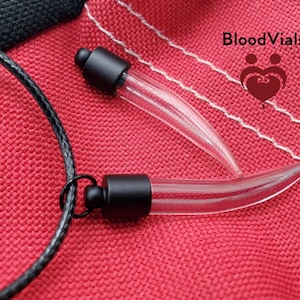 May include: Two black and clear glass vials shaped like fangs on a black cord. The vials are on a red fabric background. The text "BloodVials" is visible in the top right corner of the image.