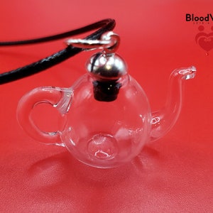 May include: A clear glass teapot-shaped pendant with a silver-colored metal cap and a black cord. The pendant is on a red background. The text "BloodVials" is visible in the upper right corner.