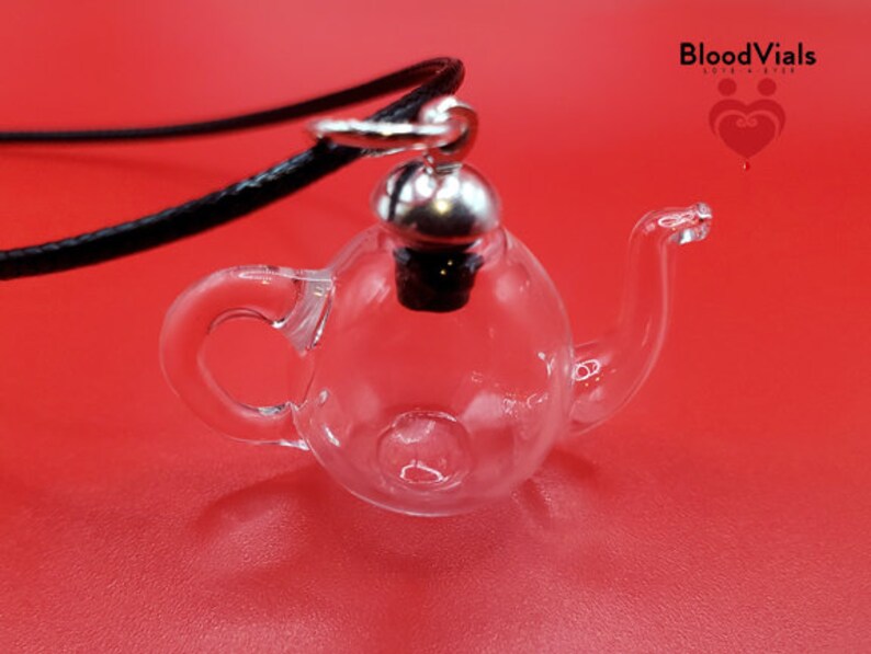 May include: A clear glass teapot-shaped pendant with a silver-colored metal cap and a black cord. The pendant is on a red background. The text "BloodVials" is visible in the upper right corner.