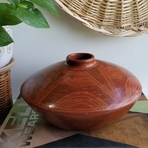 May include: A large, round, terracotta vase with a geometric design. The vase is decorated with a pattern of triangles and circles in a lighter shade of brown.