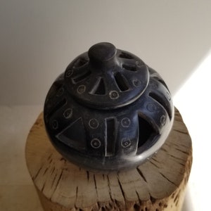 Puede incluir: Quemador de incienso de cerámica negra con intrincados diseños geométricos y patrones recortados. El quemador está sentado sobre una base de madera.