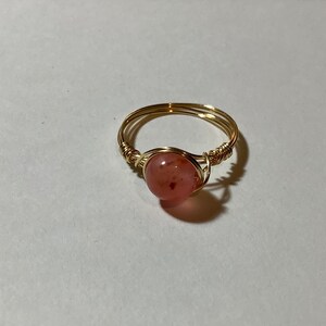May include: A gold wire wrapped ring with a pink gemstone.