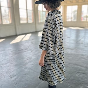 May include: A person wearing a black and white striped dress with a black hat. The dress has a loose fit and falls to the knees. The person is wearing black tights and black boots.