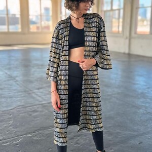 May include: A woman wearing a black and gold striped kimono with a black hat and black boots.