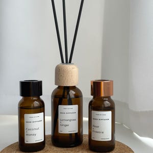 May include: Three brown glass reed diffuser bottles with black, wooden, and copper lids. The bottles are labelled with the scents "Coconut + Honey", "Lemongrass + Ginger", and "Pear + Freesia".