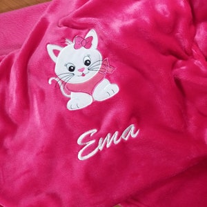 Puede incluir: Manta de forro polar rosa con un gato blanco bordado y el nombre "Ema" en ella.