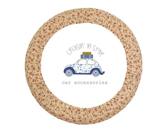 May include: A circular steering wheel cover featuring a beige fabric with a small red floral pattern. The center displays a graphic of a blue car with a blue and yellow suitcase on its roof, accompanied by the text Cruisin' in style car accessories.