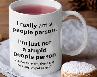 Könnte beinhalten: Ein weißer Keramikbecher mit Henkel, gefüllt mit einer rosafarbenen Flüssigkeit. Der Becher ist mit schwarzem Text bedruckt, der lautet: I really am a people person, I’m just not a stupid people person (Unfortunately, there are so many stupid people).
