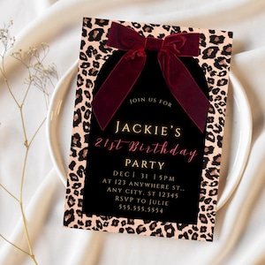 Può includere: Un invito a una festa con sfondo nero e bordo con stampa leopardata. L'invito presenta il testo "Jackie's 21st Birthday Party" in oro e rosso, con un fiocco di velluto bordeaux. L'invito è su un piatto bianco.