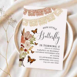 May include: A white invitation with a brown and gold paper garland, a floral bouquet with butterflies, and the text "Our Little Butterfly is Turning 1!"  Join us to celebrate Isabella's 1st Birthday! Saturday November 16th at 3:00pm. 123 Anywhere Street, Anywhere City 12345. rsvp 123-456-7890.