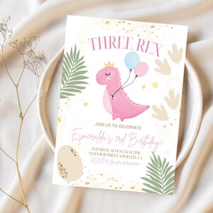 May include: A pink dinosaur with a crown and balloons, surrounded by green leaves and gold glitter. The text "THREE REX" is at the top of the card. The text "JOIN US TO CELEBRATE Esmeralda's 3rd Birthday!" is in the middle of the card. The text "SATURDAY, AUGUST 24 AT 2PM 1234 YOUR STREET, YOUR CITY, CA RSVP" is at the bottom of the card.