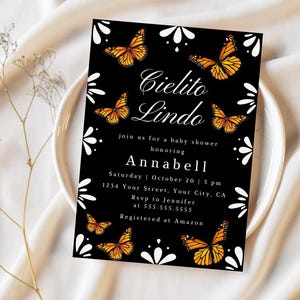 May include: Black baby shower invitation with orange butterflies and white floral accents. The invitation reads "Cielito Lindo" and announces a baby shower honoring Annabell. Includes date, time, location, and RSVP information.