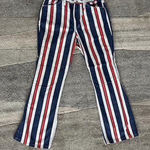 May include: Blue denim pants with vertical red and white stripes. The pants have a classic five-pocket design and a flared leg. The stripes are evenly spaced and run the full length of the pants.