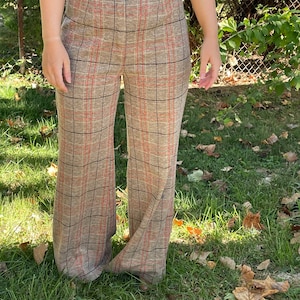 May include: Wide-leg pants with a plaid pattern in brown, orange, and black. The pants have a high waist and a button closure.