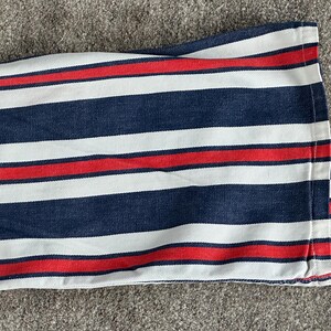May include: Close-up of a fabric with a striped pattern. The design features alternating bands of navy blue, white, and red. The fabric is folded, revealing the edge with a red stitch.