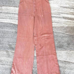 May include: Vintage high-waisted, wide-leg pants in a muted coral color. The pants feature two front pockets, a button closure, and a vertical striped texture. The pants are made of a sturdy fabric and have a classic retro style.