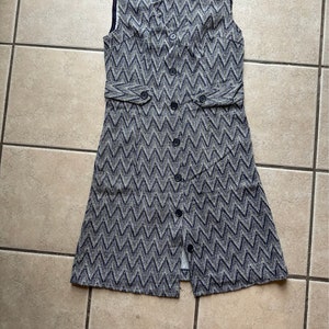 May include: A sleeveless dress with a chevron pattern in shades of blue and white. The dress has a button-up front and a fitted waist.