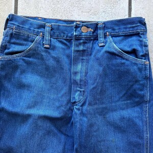 May include: A pair of dark blue denim jeans with a button fly and two front pockets. The jeans have a classic straight leg style.