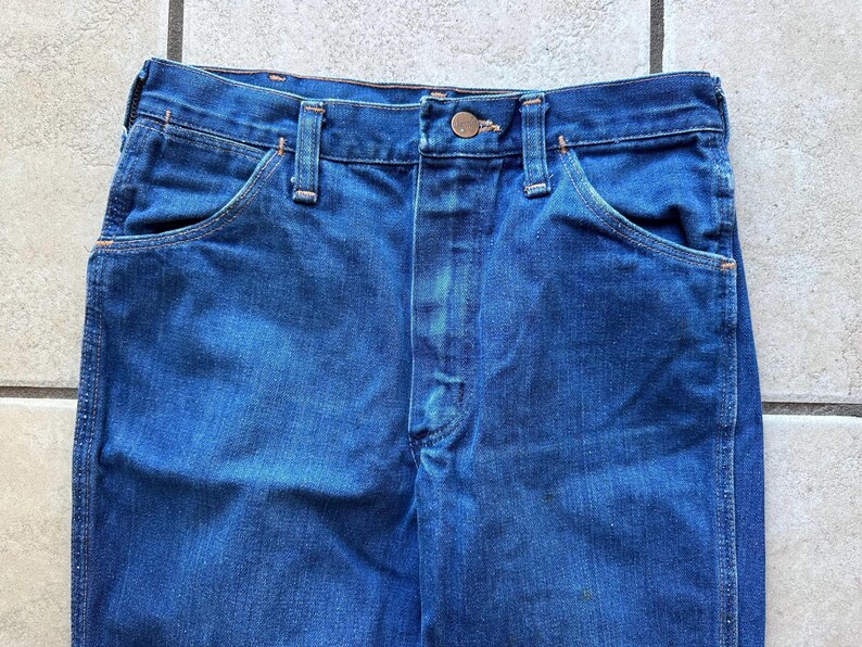 May include: A pair of dark blue denim jeans with a button fly and two front pockets. The jeans have a classic straight leg style.
