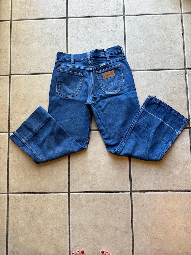 May include: A pair of blue denim jeans with a wide leg and a high waist. The jeans have a brown leather patch on the back with the Wrangler logo.