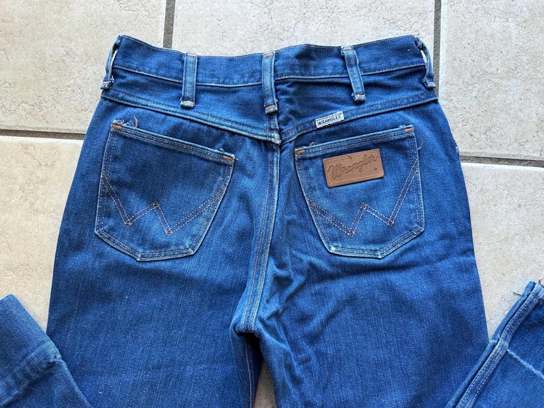 May include: A pair of blue denim jeans with a brown leather patch that says "Wrangler" on the back pocket.