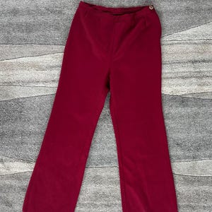 May include: A pair of burgundy corduroy pants. The pants have a high waist, a button closure, and a wide leg. The corduroy fabric has vertical ridges. The pants are a solid color and appear to be vintage.