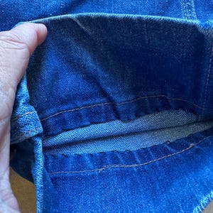 May include: Close-up of the inside of a pair of blue denim jeans, showing the double stitching along the seam.