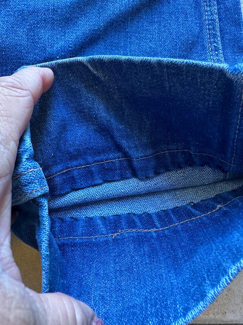 May include: Close-up of the inside of a pair of blue denim jeans, showing the double stitching along the seam.