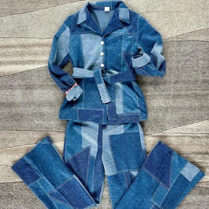 May include: A denim patchwork two-piece set featuring a collared jacket with a matching belt and flared pants. The jacket has long sleeves and button closures. The set is made of various shades of blue denim.