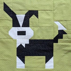 Può includere: Un blocco di patchwork nero e bianco che rappresenta un cane. Il cane è in piedi su uno sfondo verde con pois bianchi.