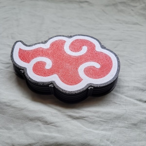Puede incluir: Un conjunto de posavasos en forma de nube roja y blanca con borde negro. Los posavasos están hechos de un material texturizado y tienen un diseño ligeramente elevado.