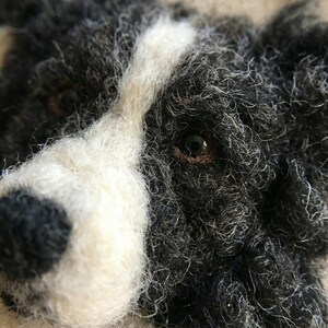 May include: Close-up of a felted dog head with black, white, and gray fur. The dog has a white stripe down its face and a dark brown eye. The fur appears textured and detailed, giving the impression of a handmade craft item.