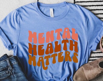May include: A blue t-shirt with the text "Mental Health Matters" in a retro font with orange, red, and pink colors.