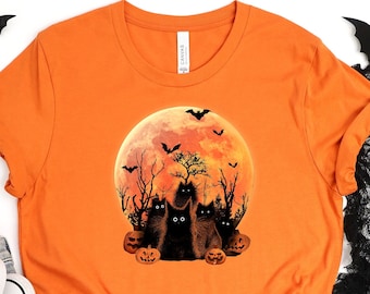 May include: Orange t-shirt with a black cat silhouette design. The cats are sitting in front of a full moon with bats flying around it. The moon is orange with black silhouettes of trees and bats.