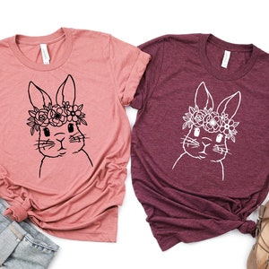 May include: Two t-shirts with a floral bunny graphic. One shirt is a dusty rose color and the other is a burgundy color.