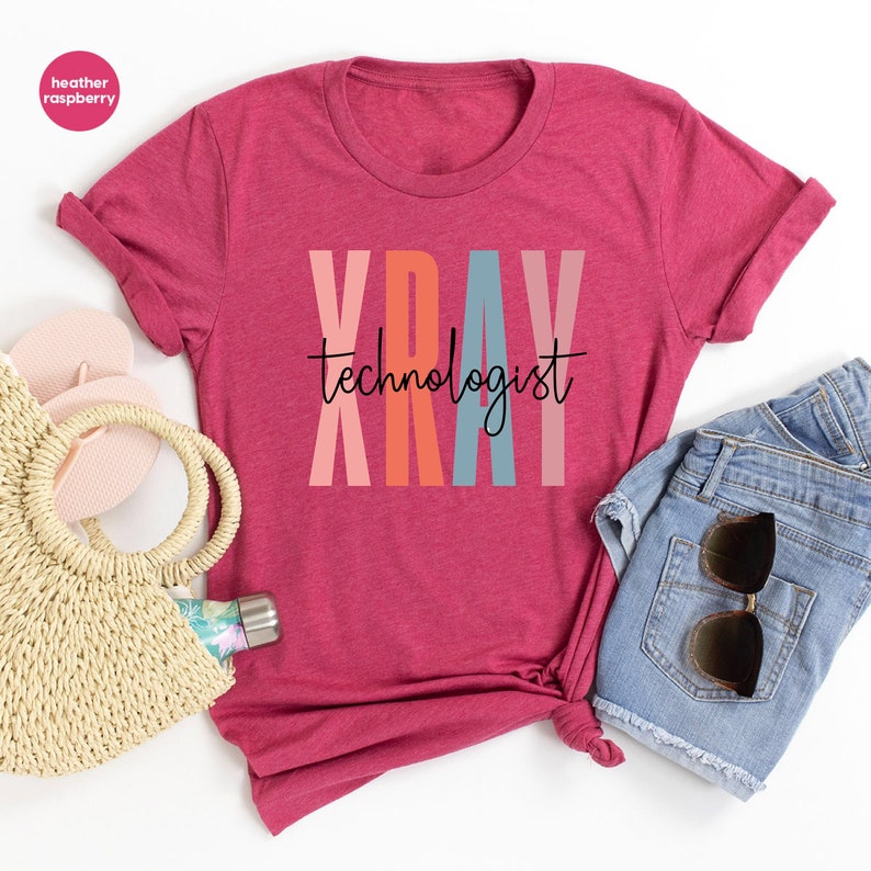 May include: A heather raspberry t-shirt with the text "XRAY technologist" in colorful letters. The letters are in shades of pink, orange, red, and blue.