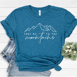 May include: A teal blue t-shirt with a white graphic of mountains and the text "Take me to the mountains".