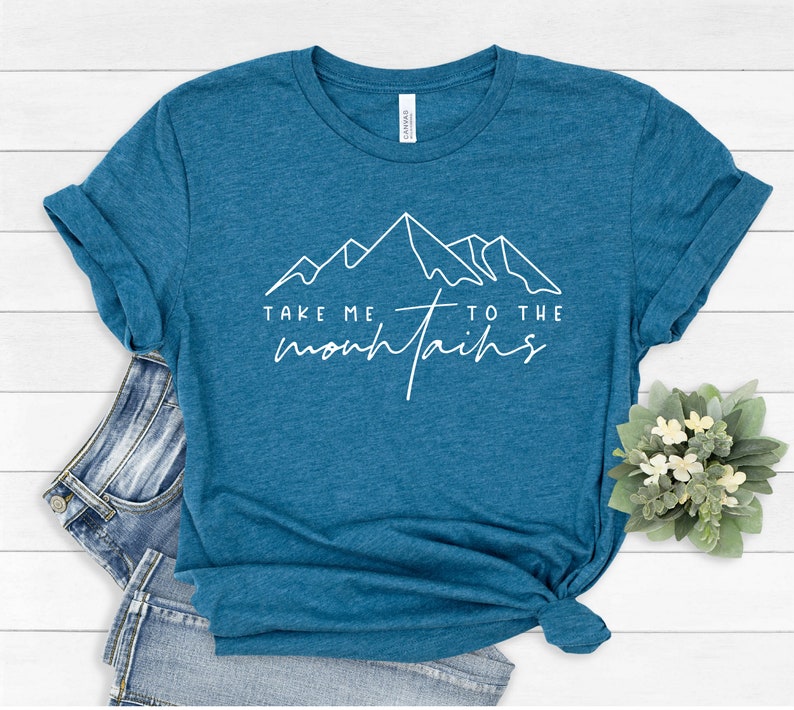 May include: A teal blue t-shirt with a white graphic of mountains and the text "Take me to the mountains".
