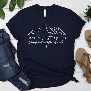 May include: A navy blue t-shirt with a white graphic of mountains and the text "Take me to the mountains".
