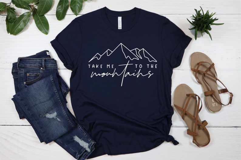 May include: A navy blue t-shirt with a white graphic of mountains and the text "Take me to the mountains".