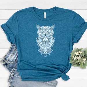 May include: A teal blue t-shirt with a white mandala-style owl graphic.