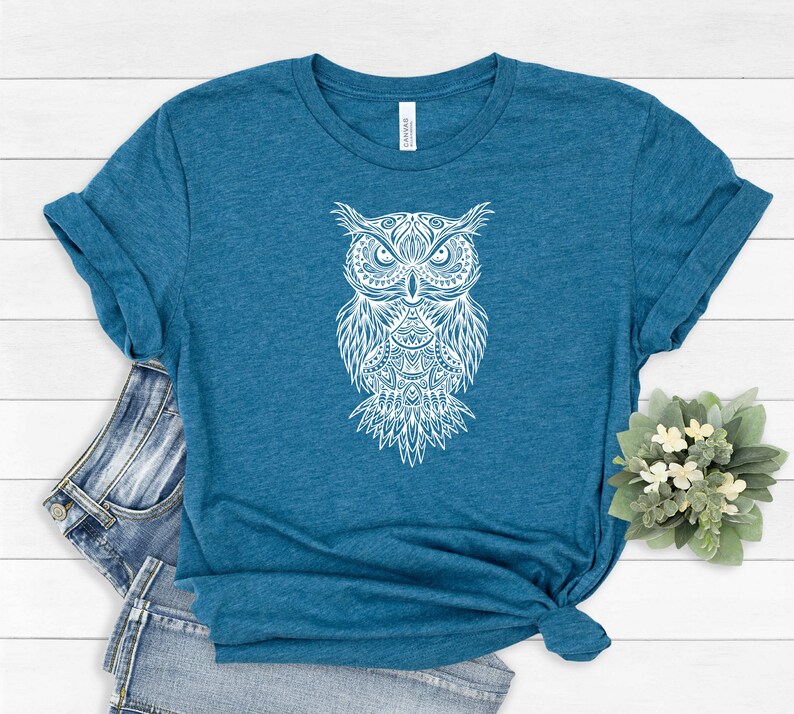 May include: A teal blue t-shirt with a white mandala-style owl graphic.