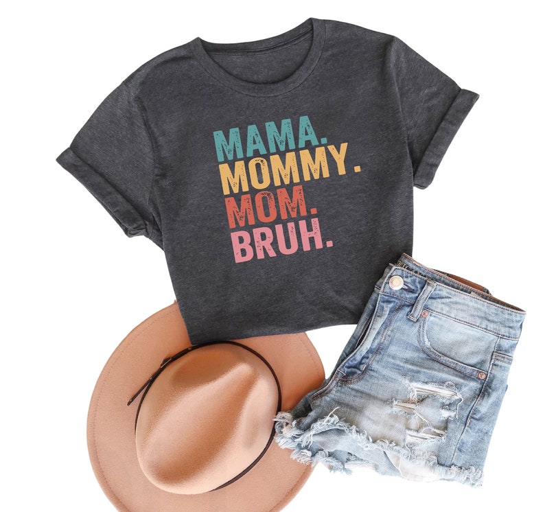 May include: A dark gray t-shirt with the text "MAMA. MOMMY. MOM. BRUH." in colorful retro-style lettering.