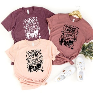 K&ouml;nnte beinhalten: Drei T-Shirts mit einem grafischen Design eines Kassettenbandes mit dem Text "80's Girls Just Wanna Have Fun" in Schwarz auf wei&szlig;em Hintergrund. Die T-Shirts sind in verschiedenen Farben: Rotbraun, Rosa und Hellrosa.