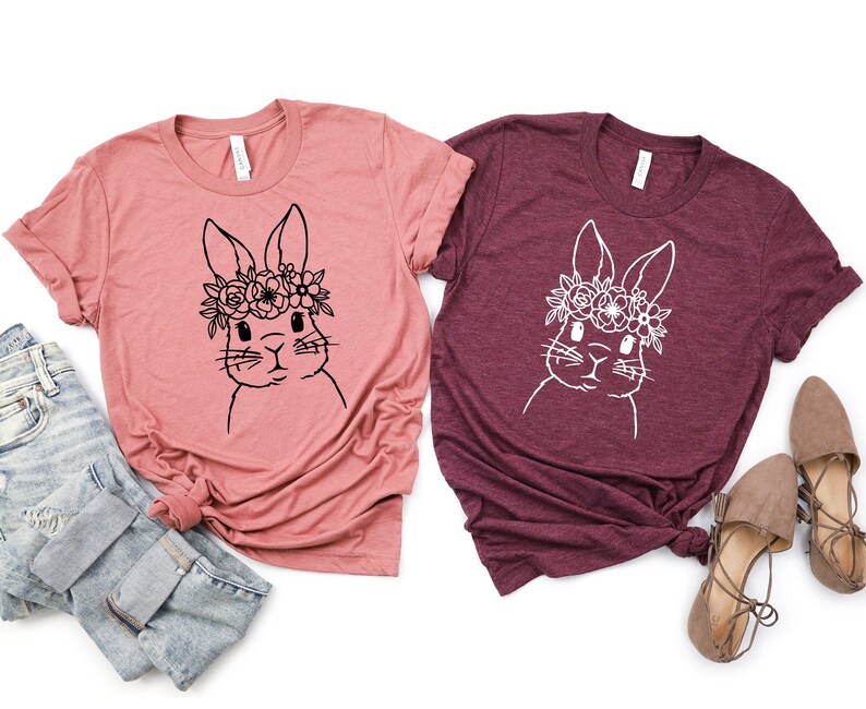 May include: Two t-shirts with a floral bunny graphic. One shirt is a dusty rose color and the other is a burgundy color.