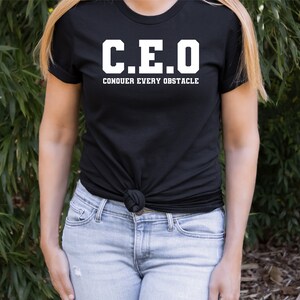 May include: Black t-shirt with white text that reads "C.E.O. CONQUER EVERY OBSTACLE"