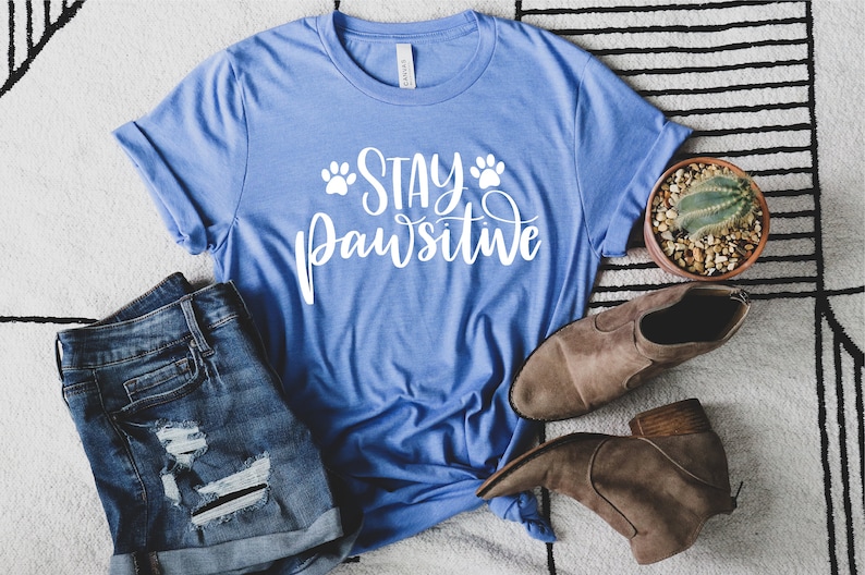 May include: A blue t-shirt with the text "Stay Pawsitive" in white lettering with paw prints on either side of the word "Stay".