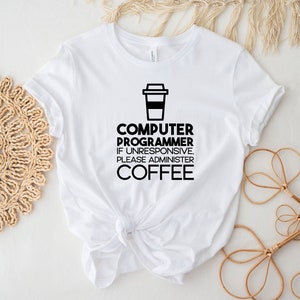 May include: White t-shirt with black text that reads "Computer Programmer. If unresponsive, please administer coffee." and a black silhouette of a coffee cup.