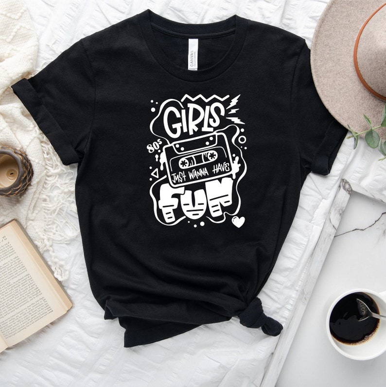 K&ouml;nnte beinhalten: Schwarzes T-Shirt mit einem wei&szlig;en Grafikdesign, das ein Kassettenband mit dem Text "80's Girls Just Wanna Have Fun" im Retro-Stil zeigt.